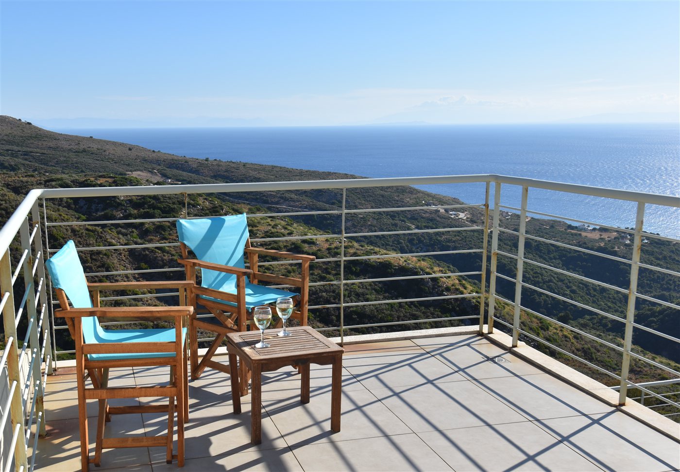 Two turquoise chairs and a glass of wine on the balcony above the hillside and sea