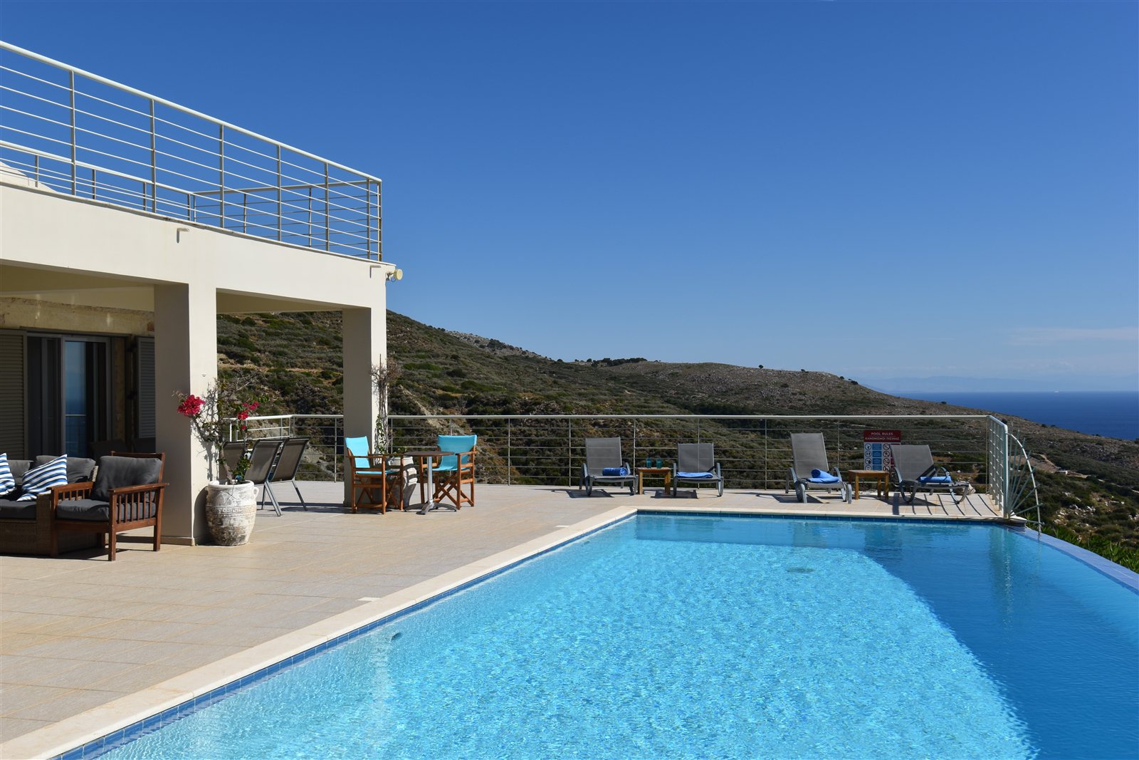 The turquoise infinity pool alongside the villa, with sun loungers and the sea beyond
