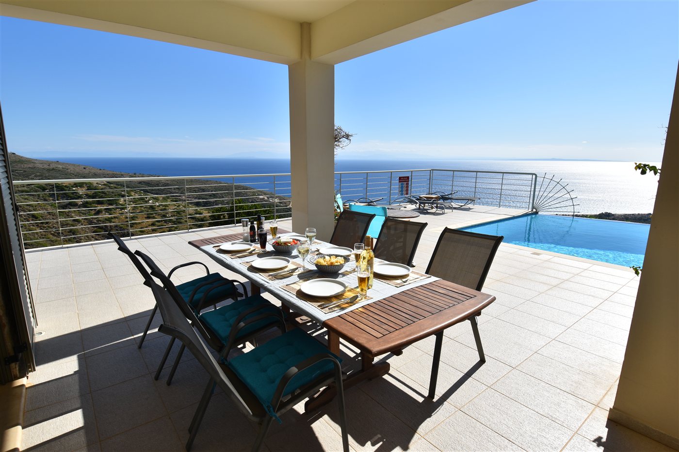 A table set for a relaxed meal on the covered terrace overlooking the pool and sea