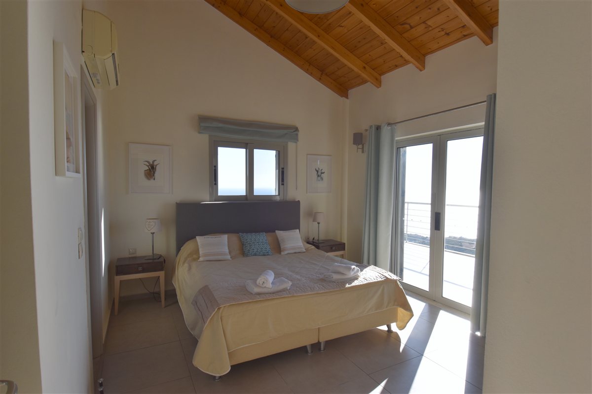 Upstairs bedroom with a high timber ceiling and doors leading to the sea-view balcony